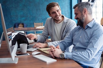 Shot of two business colleagues working in their office using a desktop computer. Man sitting at...