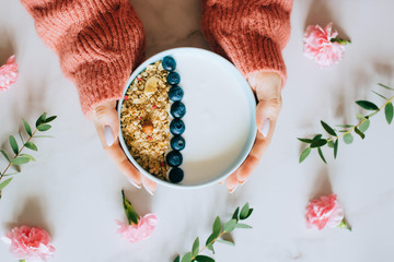 Woman in coral woolen sweater eating breakfast bowl with muesli and yogurt, berries and hazelnuts. Clean eating, vegetarian, vegan, alkiline diet food concept