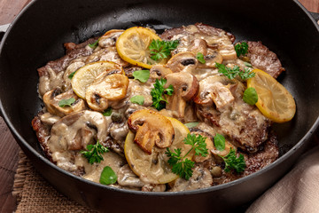 A closeup photo of scallopine di vitello, veal scallopini, a traditional Italian dish with a mushroom sauce, lemons, and parsley, in a dutch oven - obrazy, fototapety, plakaty