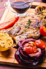 Juicy pork steak with a sprig of fresh thyme, lemon and grilled vegetables and sauce served on a wooden board