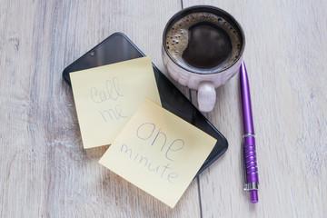 Smartphone with a sticky note sheet with an inscription  call me and one minute,a cup of coffee and...
