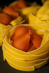 Yellow tagliatelle and red raw shells on black background