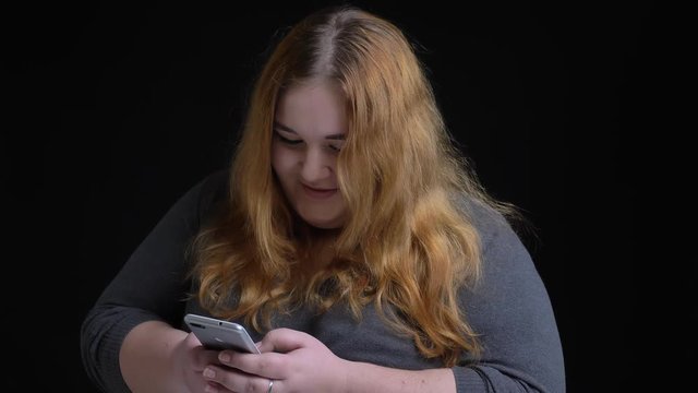 Closeup shoot of young overweight caucasian female using the phone then looking at camera and smiling