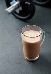 Chocolate Protein Shake and Dumbbells. Nutrition for bodybuilding. Black stone background. Copy space.