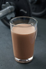 Chocolate Protein Shake and Dumbbells. Nutrition for bodybuilding. Black stone background. Copy space.