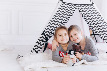 Two positive cheerful girls playing together at home with toys in children wigwam. Friendship, childhood, happiness concept