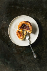 Broken Traditional Portuguese egg tart dessert Pasteis Pastel de nata on ceramic plate with fork over dark metal background. Flat lay, space