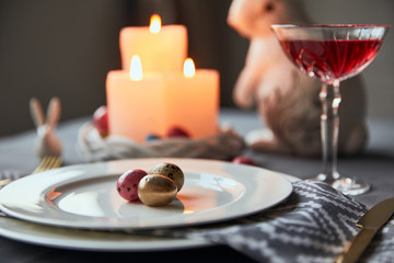 selective focus of plates with eggs, wine in crystal glass, burning candles and decorative bunnies on table at home