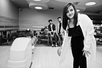 South asian woman standing at bowling alley with ball on hands. Girl is preparing for a throw.