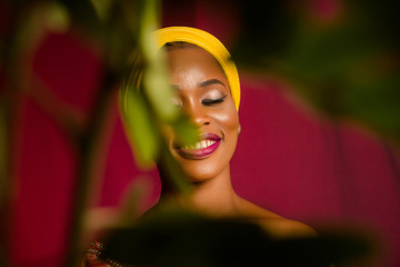 Portrait of a lady wearing yellow scarf on red background with some blurred flowers in the foreground. 