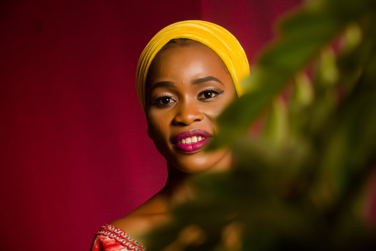 Portrait of a lady wearing yellow scarf on red background with some blurred flowers in the foreground. 