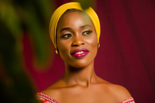 Portrait of a lady wearing yellow scarf on red background with some blurred flowers in the foreground. 