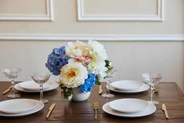 plates, knifes and forks, crystal glasses and bouquet in white vase on wooden table in restaurant