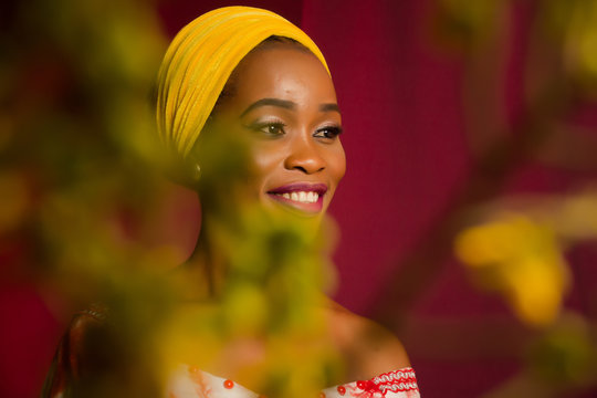 Portrait of a lady wearing yellow scarf on red background with some blurred flowers in the foreground. 