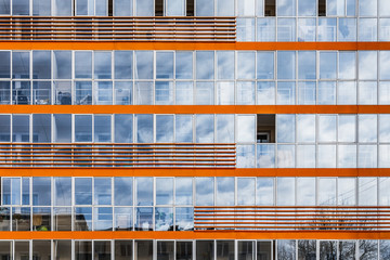 A new modern building of student dormitorie in the campus with many windows with reflections of blue sky with white clouds. Horisontal texture of blue windows and orange decore