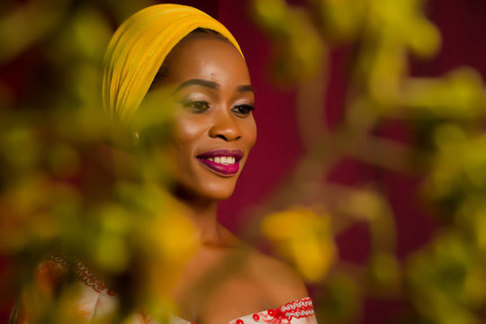 Portrait of a lady wearing yellow scarf on red background with some blurred flowers in the foreground. 