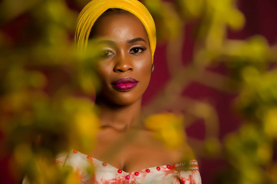 Portrait of a lady wearing yellow scarf on red background with some blurred flowers in the foreground. 