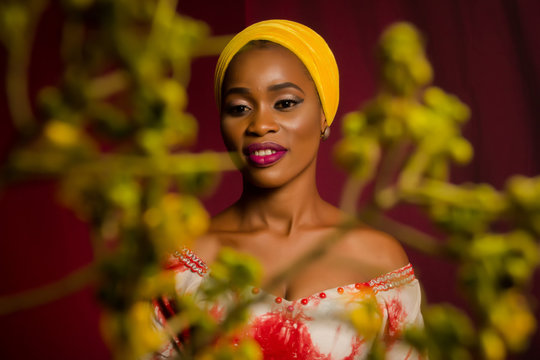 Portrait of a lady wearing yellow scarf on red background with some blurred flowers in the foreground. 