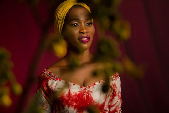 Portrait of a lady wearing yellow scarf on red background with some blurred flowers in the foreground. 