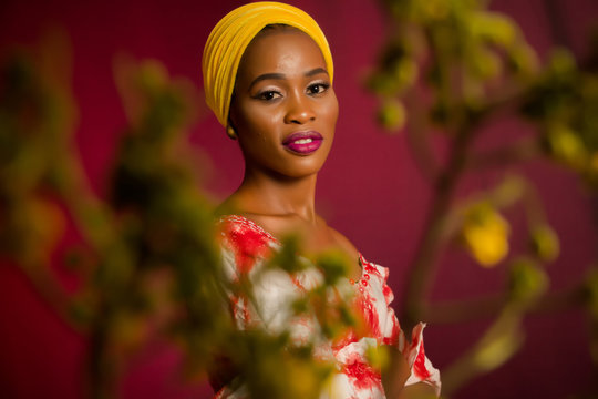Portrait of a lady wearing yellow scarf on red background with some blurred flowers in the foreground. 