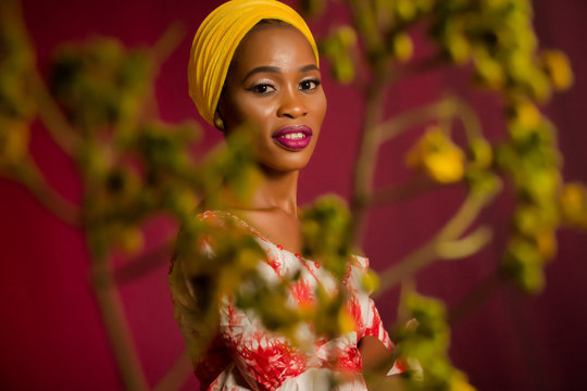 Portrait of a lady wearing yellow scarf on red background with some blurred flowers in the foreground. 
