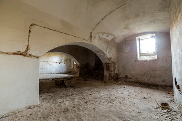Fototapeta na wymiar Old forsaken empty basement room of ancient building or palace with cracked plastered brick walls, low arched ceiling, small windows with iron bars and dirty floor.