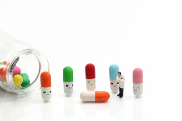Miniature people: doctor standing with colorful pills and drug bottle isolated on white background. Healthcare, medical service, and insurance concept
