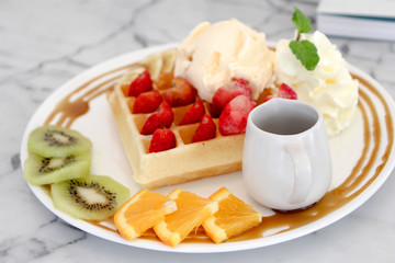 Belgium waffles with strawberries and ice cream on white plate.