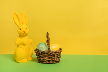 Yellow decoration easter bunny with a basket with eggs on a yellow and green background with copy space