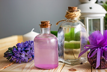 Floral cosmetic water for the face in a transparent bottle stands in the center of the wooden table, in the background there is a transparent white bottle, a purple hyacinth flower