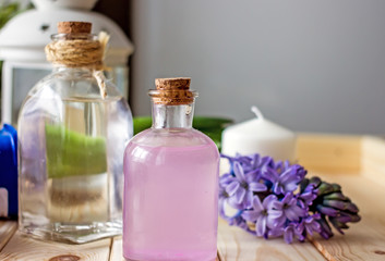 Fototapeta na wymiar Floral cosmetic water for the face in a transparent bottle stands in the center of the wooden table, in the background there is a transparent white bottle, a purple hyacinth flower