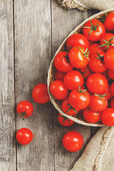 Fresh red tomatoes in a wicker basket on an old wooden table. Ripe and juicy cherry tomatoes with drops of moisture, gray wooden table, around a cloth of burlap. In a rustic style.