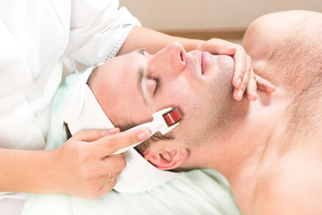 The man undergoes the procedure of medical micro needle therapy with a modern medical instrument derma roller. 