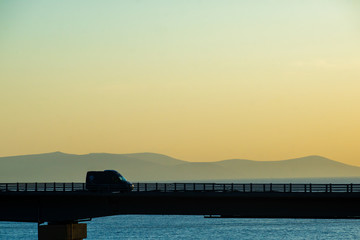Obraz premium Cars on the highway bridge during the dawn against the backdrop of mountains and the sea
