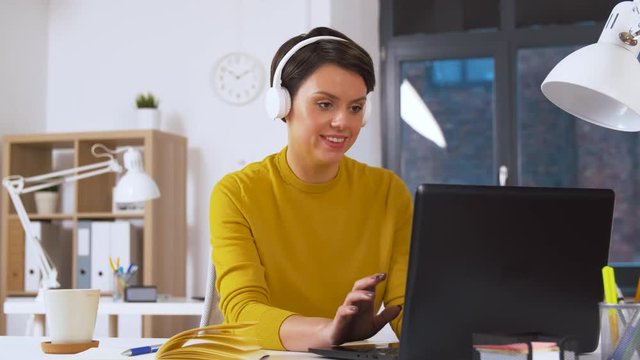 business, technology and people concept - happy creative woman in headphones with laptop computer working and listening to music at office
