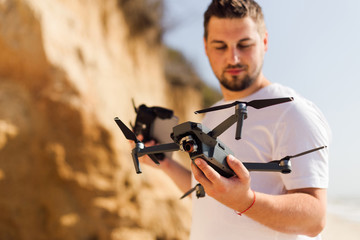Young man holding drone before flight near ocean or sea. Pretty guy prepare to pilot outdoor