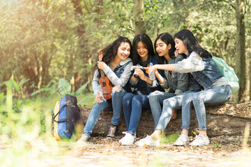 Fototapeta na wymiar Talking happily after hiking.A group of Asian women are sitting and resting from walking in the forest and looking at pictures from the camera happily.