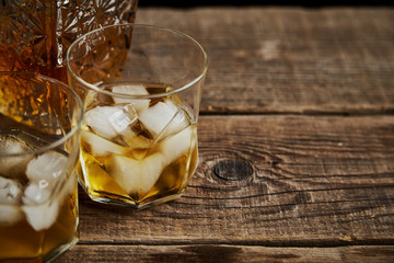 Whiskey with ice in glasses, rustic wood background, copy space 