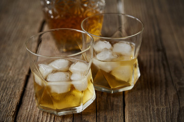 Whiskey with ice in glasses, rustic wood background, copy space 