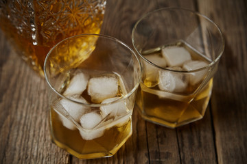 Whiskey with ice in glasses, rustic wood background, copy space 