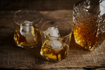 Whiskey with ice in glasses, rustic wood background, copy space 
