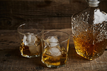 Whiskey with ice in glasses, rustic wood background, copy space 