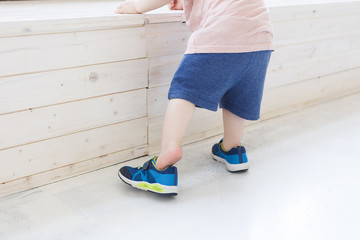 Сute little toddler learn to dress shoes while leaning on the wooden podium. Сoncept of caring for kids