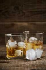 Whiskey with ice in glasses, rustic wood background, copy space 