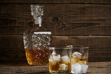 Whiskey with ice in glasses, rustic wood background, copy space 