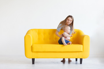 Portrait of loving young mother playing with her kid. Playful woman holding little cute son. Calm caring mommy has playful state of mind and happy mood, making her child smile. Yellow sofa