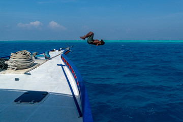maldivian man jumping in water and diving from boat