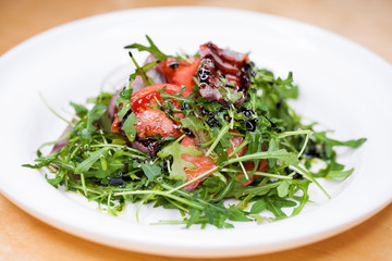 Salad with pieces of marbled beef and arugula on a white plate