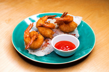 Deep fried king prawns with spicy sauce on a blue plate