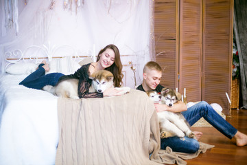 Joyful young loving couple sitting in the bedroom while expressing love with Malamute puppies 